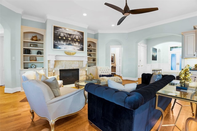 living room with ceiling fan, built in features, crown molding, light hardwood / wood-style floors, and a fireplace