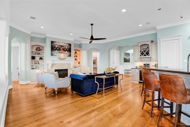 living room featuring built in shelves, ceiling fan, light hardwood / wood-style floors, bar, and ornamental molding