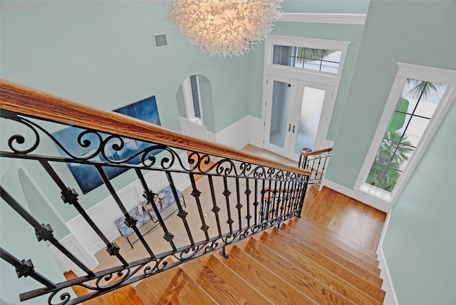 staircase featuring hardwood / wood-style floors, french doors, a high ceiling, and a chandelier