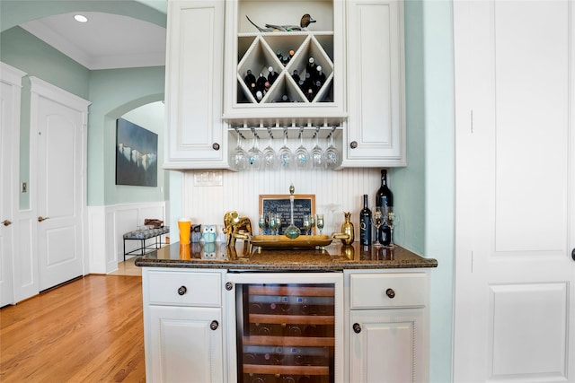 bar featuring dark stone countertops, white cabinetry, beverage cooler, and light wood-type flooring