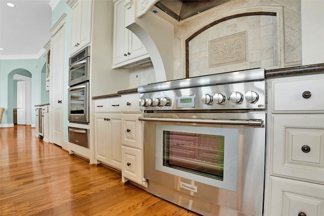 kitchen with light hardwood / wood-style flooring, ornamental molding, tasteful backsplash, white cabinetry, and stainless steel appliances