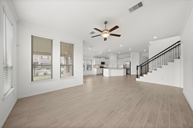 unfurnished living room with ceiling fan, light hardwood / wood-style floors, ornamental molding, and sink