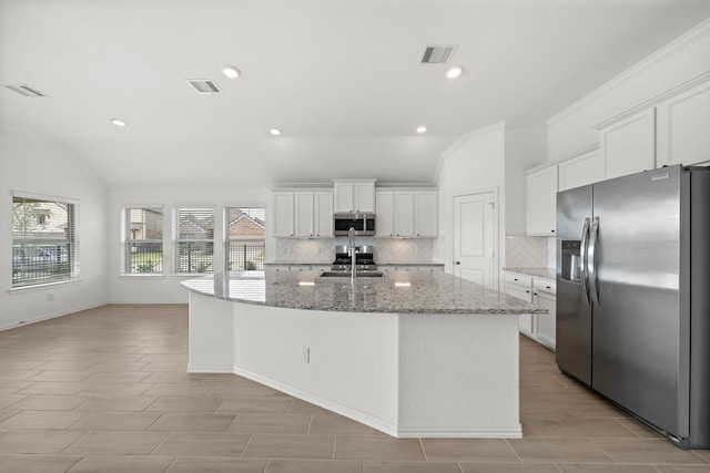 kitchen with lofted ceiling, a kitchen island with sink, stone counters, appliances with stainless steel finishes, and white cabinetry