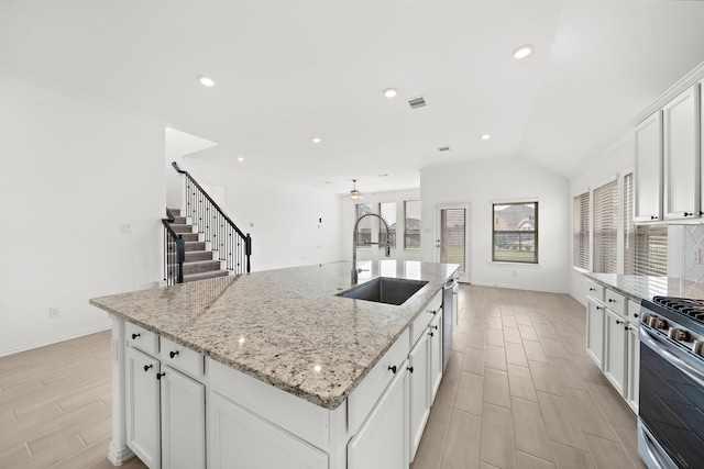 kitchen featuring appliances with stainless steel finishes, sink, white cabinets, lofted ceiling, and an island with sink