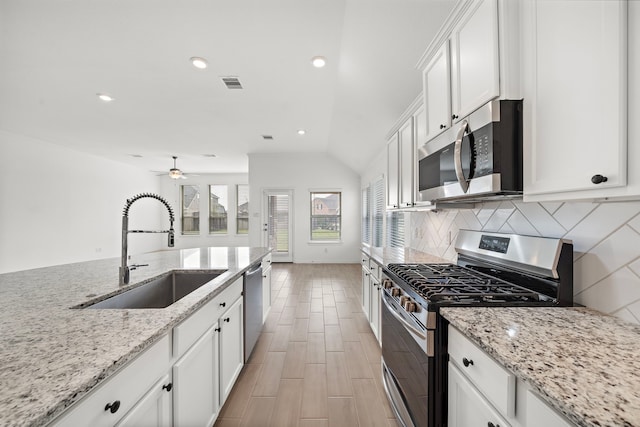 kitchen with sink, light stone counters, lofted ceiling, white cabinets, and appliances with stainless steel finishes