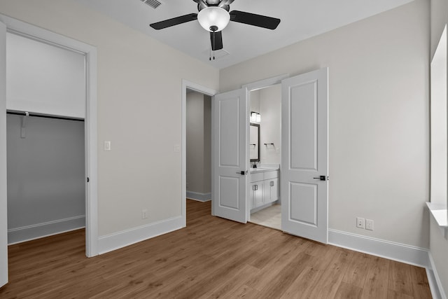 unfurnished bedroom with ensuite bath, a spacious closet, light wood-type flooring, a closet, and ceiling fan