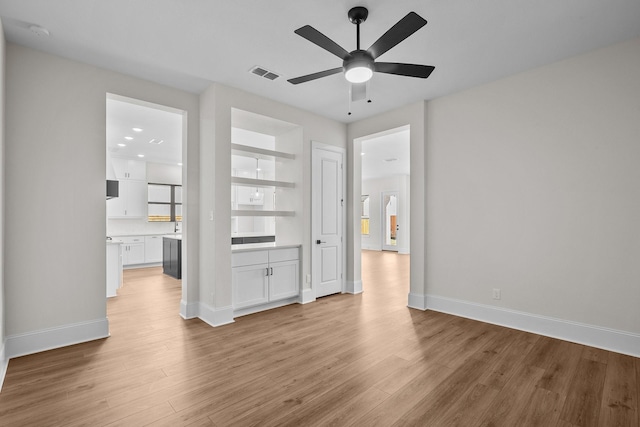 unfurnished living room featuring built in shelves, light hardwood / wood-style flooring, and ceiling fan