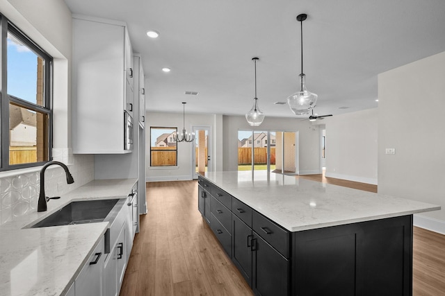 kitchen with ceiling fan with notable chandelier, pendant lighting, white cabinetry, decorative backsplash, and a center island