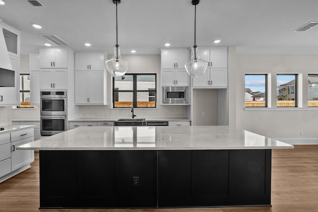 kitchen with a spacious island, appliances with stainless steel finishes, pendant lighting, light stone countertops, and white cabinets