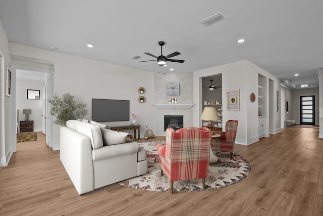 living room featuring a tile fireplace, ceiling fan, and light hardwood / wood-style floors