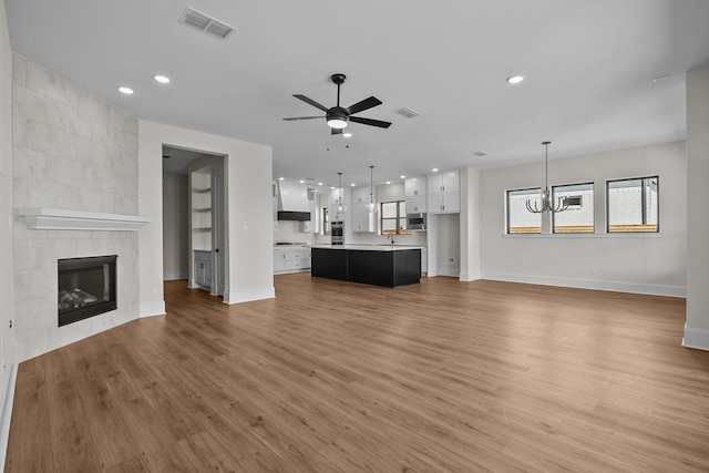 unfurnished living room with hardwood / wood-style flooring, a tile fireplace, sink, and ceiling fan with notable chandelier