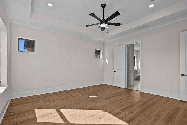 empty room with hardwood / wood-style flooring, ceiling fan, a tray ceiling, and crown molding