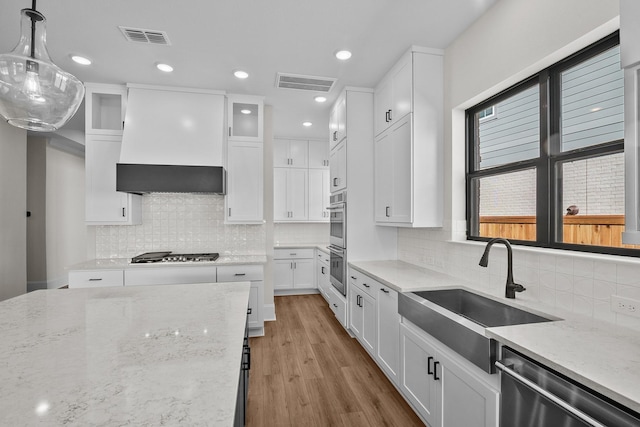 kitchen featuring premium range hood, white cabinets, hanging light fixtures, stainless steel appliances, and light wood-type flooring