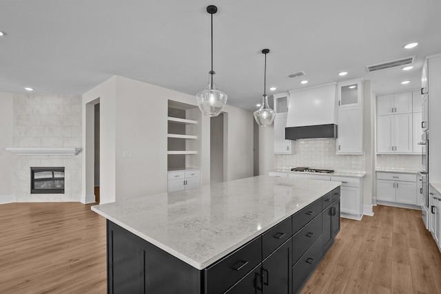 kitchen with a large island, a tile fireplace, white cabinetry, decorative light fixtures, and custom exhaust hood