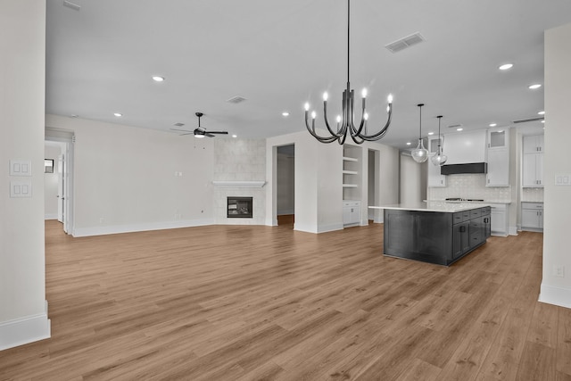 kitchen with a tile fireplace, hanging light fixtures, a center island, white cabinets, and ceiling fan with notable chandelier