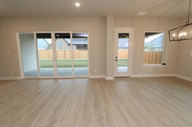 unfurnished room featuring an inviting chandelier, a healthy amount of sunlight, and light wood-type flooring