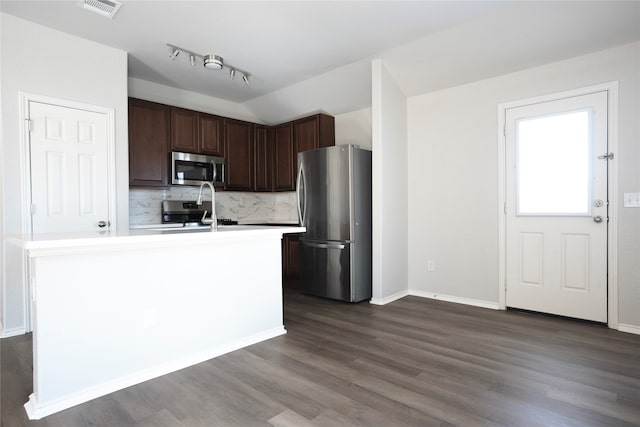 kitchen with dark wood-type flooring, decorative backsplash, an island with sink, appliances with stainless steel finishes, and dark brown cabinets