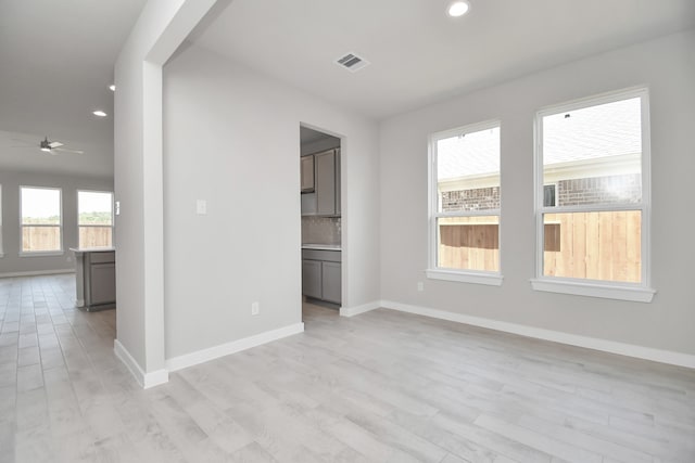 empty room with ceiling fan, a healthy amount of sunlight, and light wood-type flooring