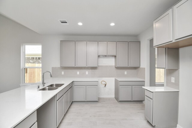 kitchen featuring gray cabinetry, backsplash, light hardwood / wood-style floors, and sink