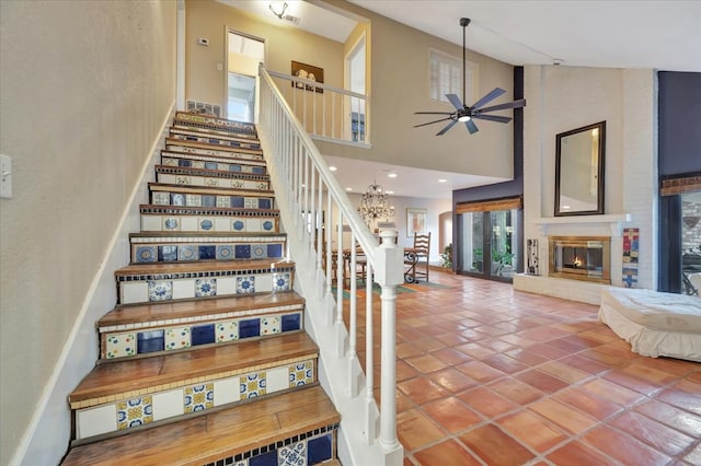 stairs featuring tile patterned flooring, a towering ceiling, and ceiling fan with notable chandelier