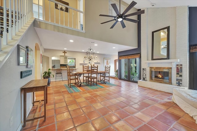 tiled dining area featuring a fireplace, ceiling fan with notable chandelier, and a high ceiling