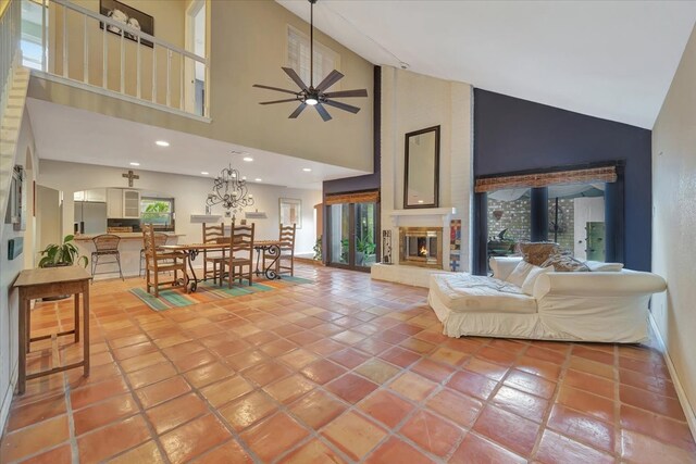 tiled living room featuring ceiling fan, a large fireplace, a wood stove, and high vaulted ceiling