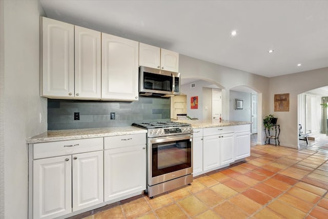 kitchen featuring tasteful backsplash, light stone countertops, white cabinets, and stainless steel appliances