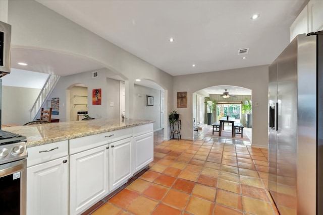 kitchen featuring white cabinets, appliances with stainless steel finishes, light stone counters, and ceiling fan