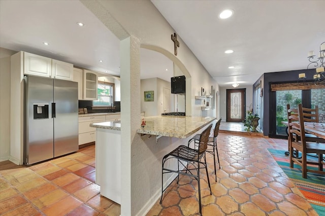 kitchen featuring a kitchen breakfast bar, kitchen peninsula, stainless steel fridge with ice dispenser, light stone counters, and white cabinetry