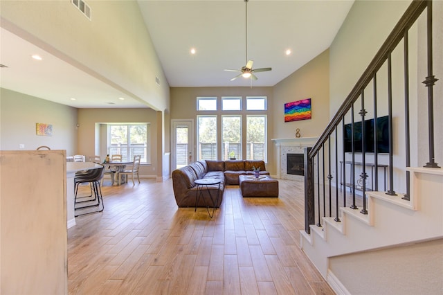 living room with ceiling fan, a tiled fireplace, high vaulted ceiling, and light hardwood / wood-style floors