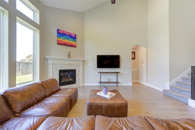 living room with a towering ceiling, light hardwood / wood-style flooring, a wealth of natural light, and a tiled fireplace