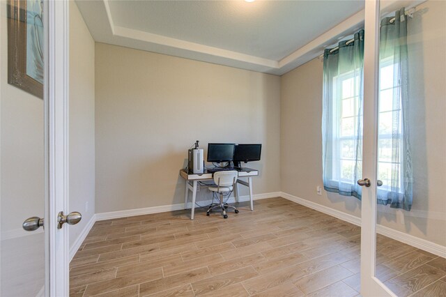 home office featuring a raised ceiling, french doors, and light hardwood / wood-style floors