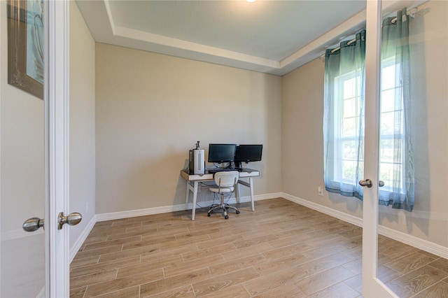 office featuring a tray ceiling, light wood-type flooring, and french doors