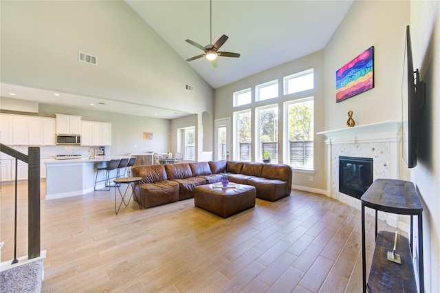 living room with a tile fireplace, high vaulted ceiling, light hardwood / wood-style flooring, and ceiling fan