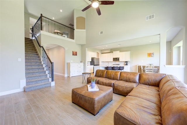 living room with a high ceiling, light wood-type flooring, and ceiling fan