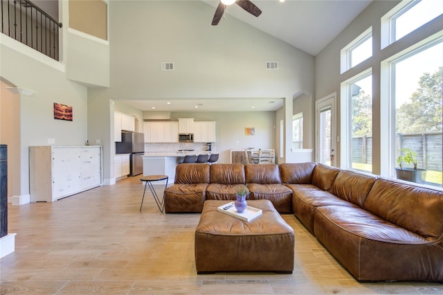 living room featuring ceiling fan, a high ceiling, and light hardwood / wood-style flooring