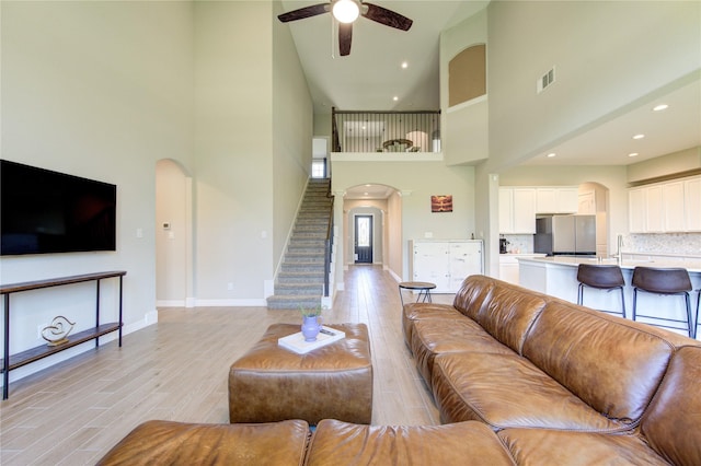 living room featuring a high ceiling, light wood-type flooring, ceiling fan, and sink