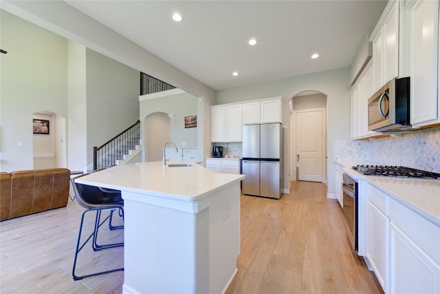 kitchen with stainless steel appliances, a kitchen island with sink, sink, white cabinetry, and a kitchen bar