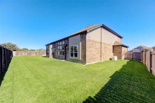 rear view of house with central AC unit and a lawn