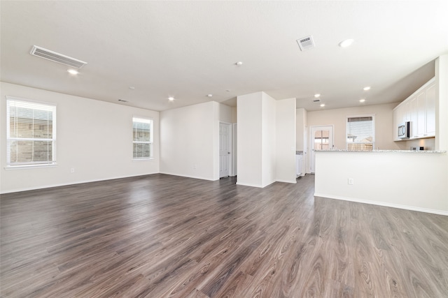 unfurnished living room featuring a wealth of natural light and dark wood-type flooring