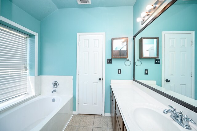 bathroom with tile patterned flooring, a tub to relax in, a textured ceiling, vaulted ceiling, and vanity