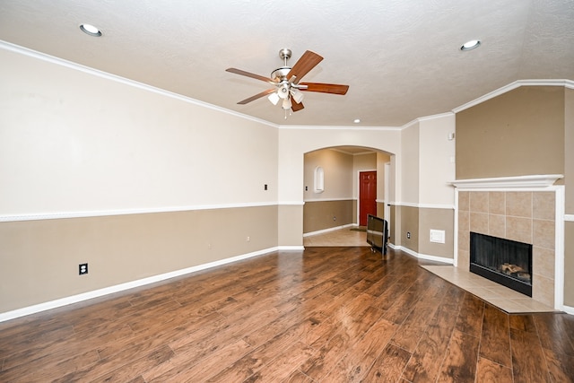 unfurnished living room with ornamental molding, a textured ceiling, ceiling fan, a tile fireplace, and hardwood / wood-style floors