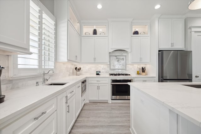 kitchen with white cabinetry, sink, light stone counters, light hardwood / wood-style floors, and appliances with stainless steel finishes