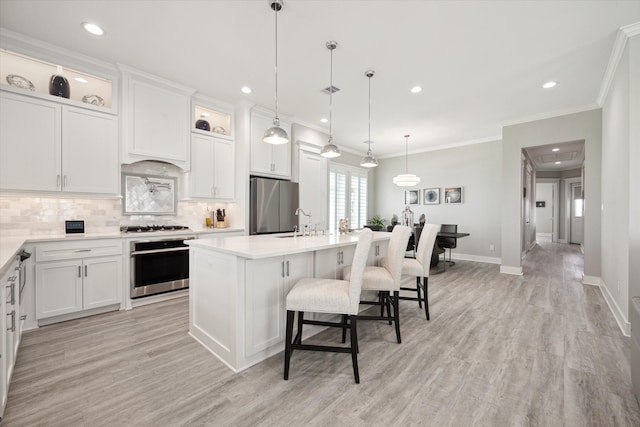 kitchen featuring pendant lighting, a center island with sink, white cabinets, light hardwood / wood-style flooring, and stainless steel appliances