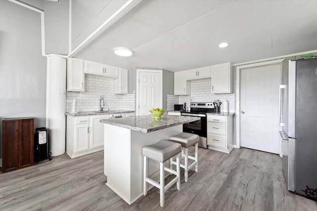 kitchen with white cabinets, light stone countertops, light hardwood / wood-style floors, appliances with stainless steel finishes, and a kitchen island