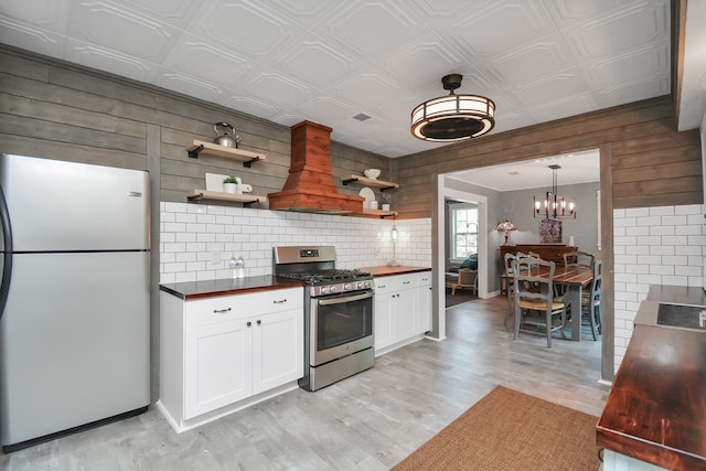 kitchen featuring white cabinets, white refrigerator, gas stove, and wood walls