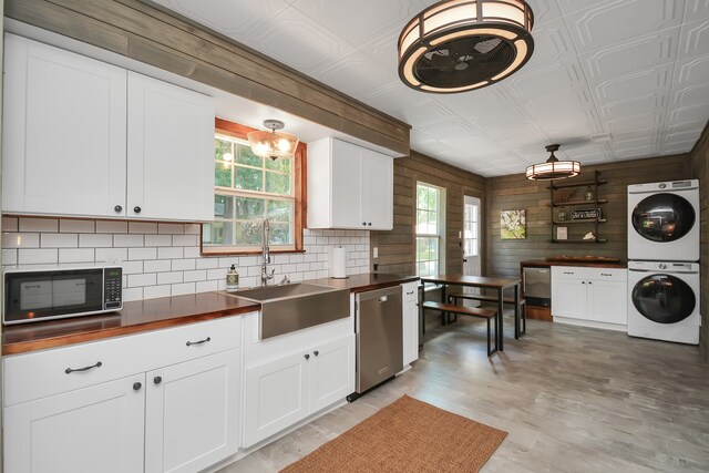 kitchen with a wealth of natural light, stacked washer and dryer, stainless steel dishwasher, and wood walls