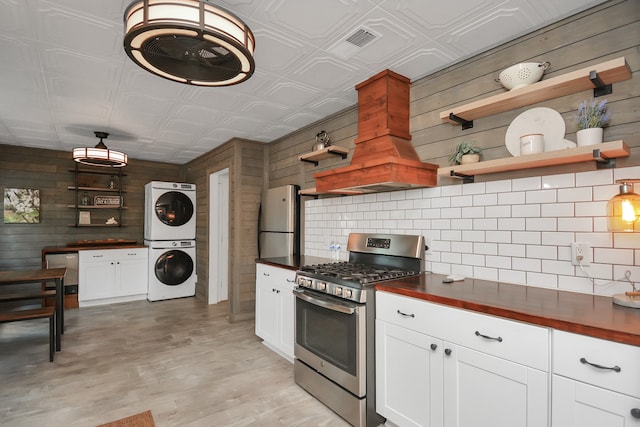 kitchen featuring white cabinetry, light hardwood / wood-style flooring, stacked washer / dryer, wooden walls, and appliances with stainless steel finishes