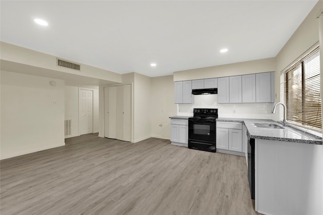 kitchen with sink, black appliances, light hardwood / wood-style flooring, dark stone countertops, and gray cabinets