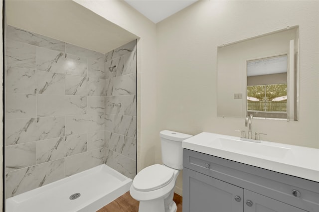 bathroom with wood-type flooring, vanity, a tile shower, and toilet